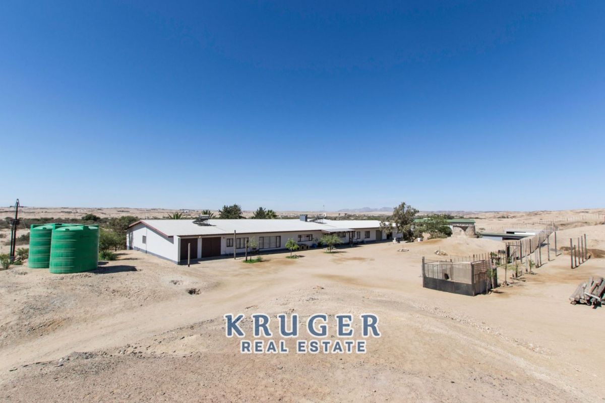 Aerial view of a small holding property featuring a main dwelling, large water storage tanks, and expansive surrounding land in an arid landscape.