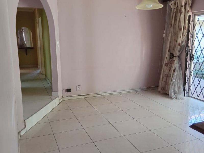 An empty living room featuring ceramic floor tiles, an arched entryway, and a sliding glass door with a security gate leading to the exterior.