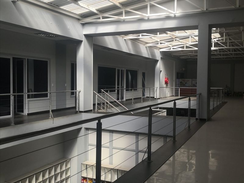 Spacious industrial mezzanine level featuring a high-clearance steel truss roof with integrated skylights, polished tiled flooring, and modern stainless steel balustrades.
