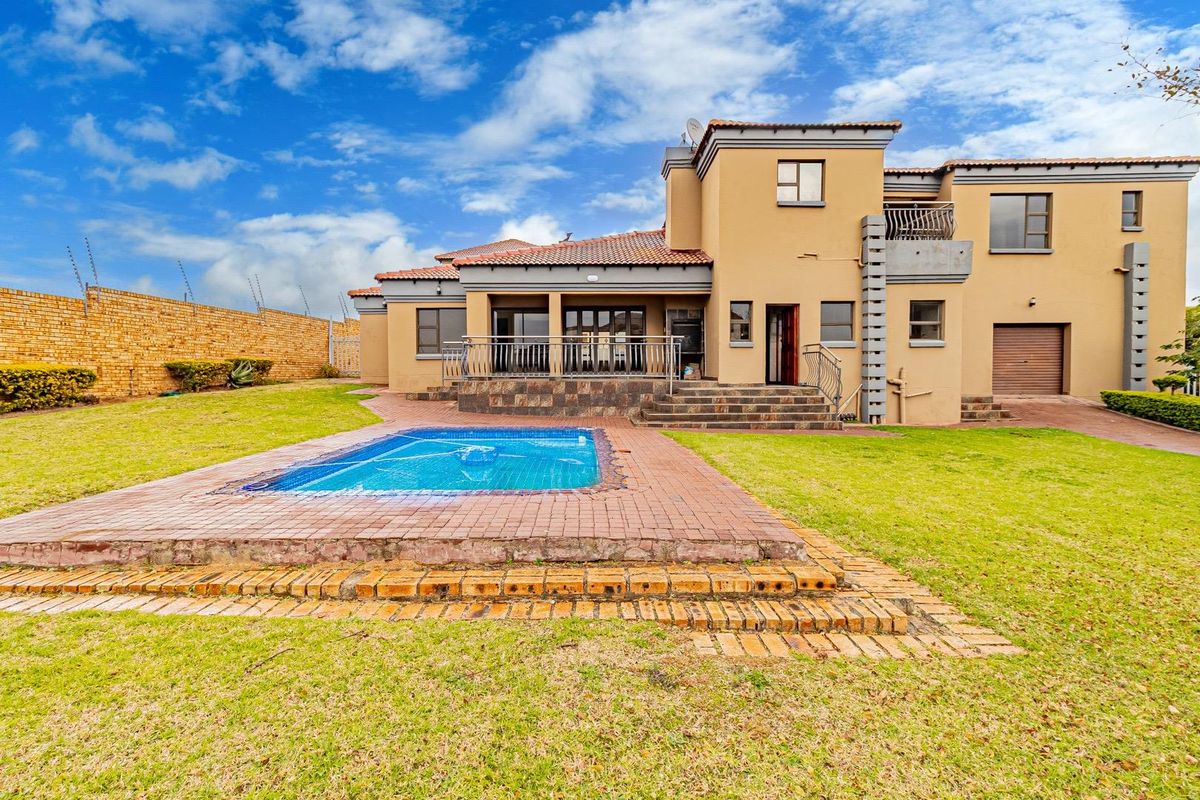 Rear view of a multi-story house featuring a swimming pool, paved patio area, and a spacious garden with perimeter walling.