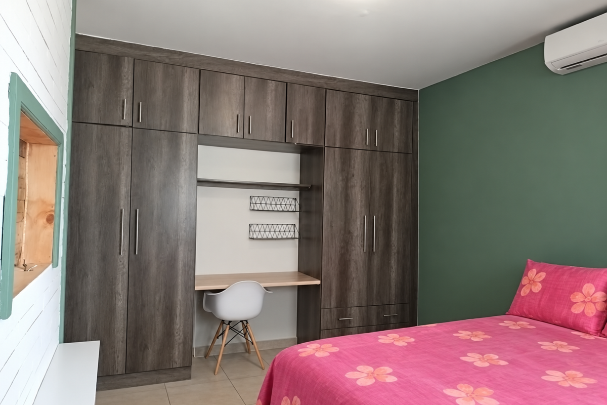 A well-maintained bedroom featuring extensive dark wood built-in cabinetry with an integrated desk, tiled flooring, and a wall-mounted air conditioning unit.