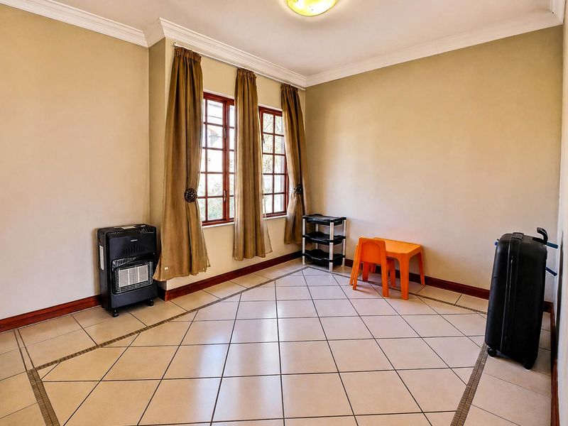 A bright, neutrally painted living area featuring tiled flooring, crown molding, and large windows that allow for ample natural light.
