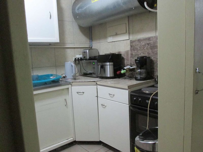 A compact kitchen featuring dated white cabinetry, a tiled backsplash, and a wall-mounted geyser, providing essential functional space for meal preparation.