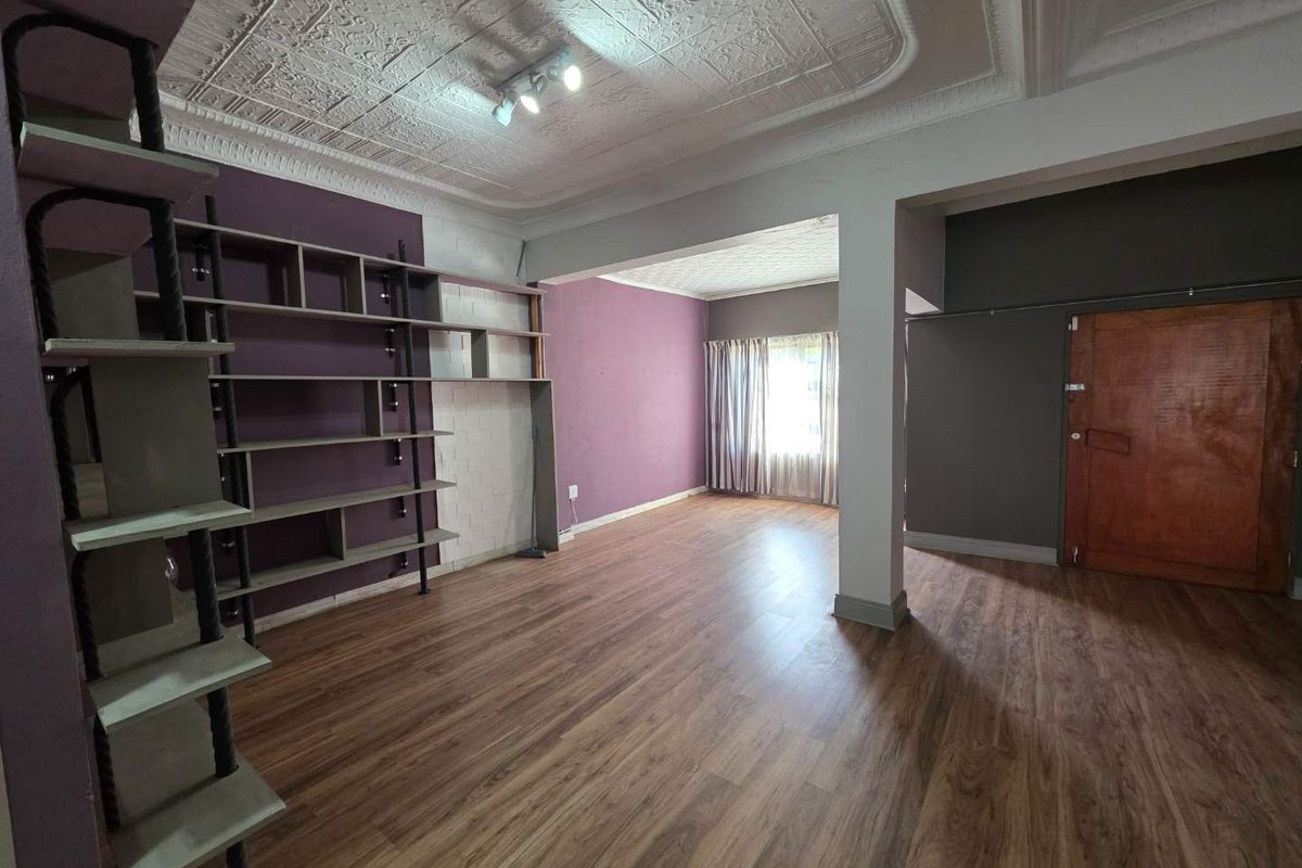 Spacious living area featuring wood-look laminate flooring, decorative pressed metal ceiling, and built-in shelving units.