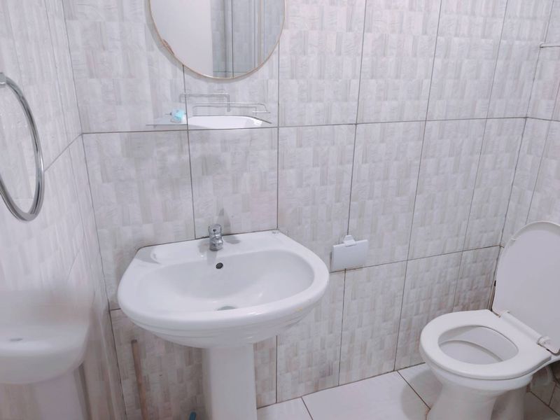 A compact bathroom featuring a pedestal basin, toilet, and neutral wall tiling throughout.