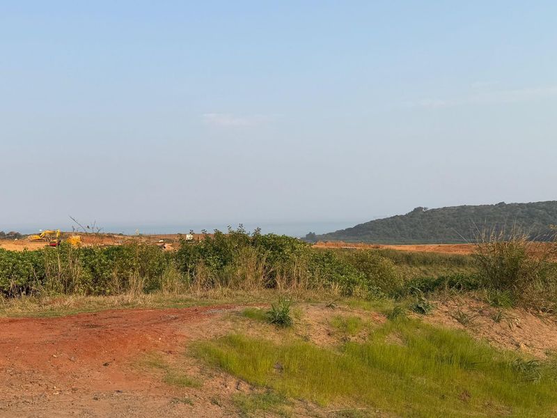 A wide-angle view of undeveloped residential land featuring natural coastal terrain and distant hillside scenery.