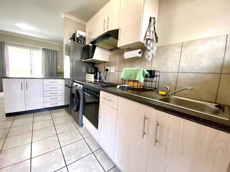 Functional kitchen featuring light wood-finish cabinetry, dark laminate countertops, integrated oven and hob, and tiled flooring with a neutral backsplash.