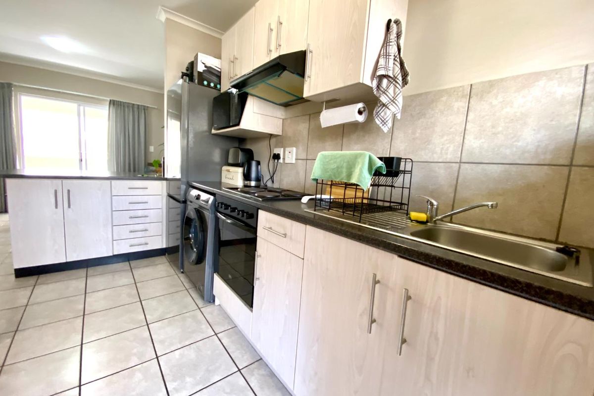 Functional kitchen featuring light wood-finish cabinetry, dark laminate countertops, integrated oven and hob, and tiled flooring with a neutral backsplash.