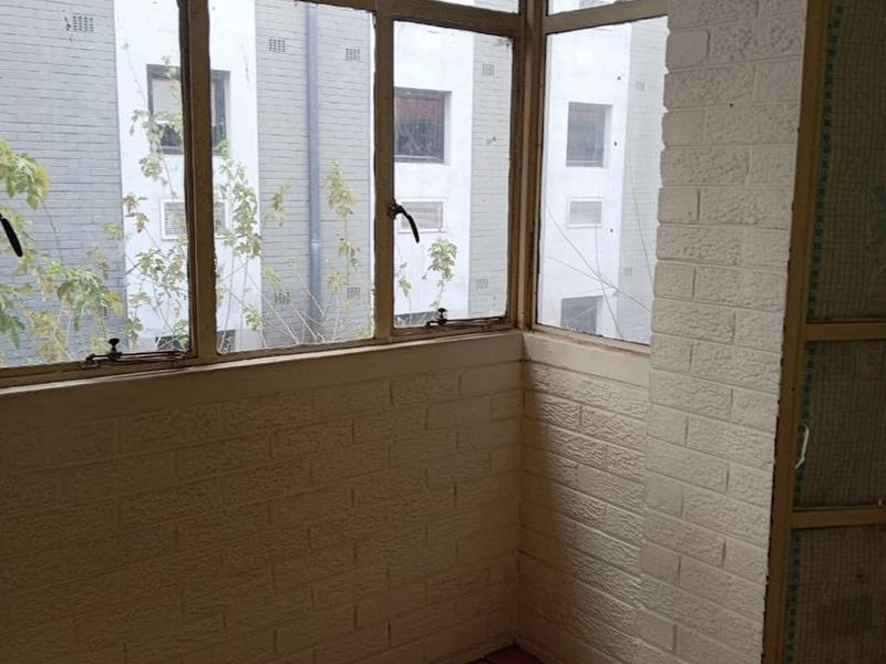 An enclosed balcony or sunroom featuring tiled flooring, painted brick walls, and large metal-framed windows overlooking the adjacent building.