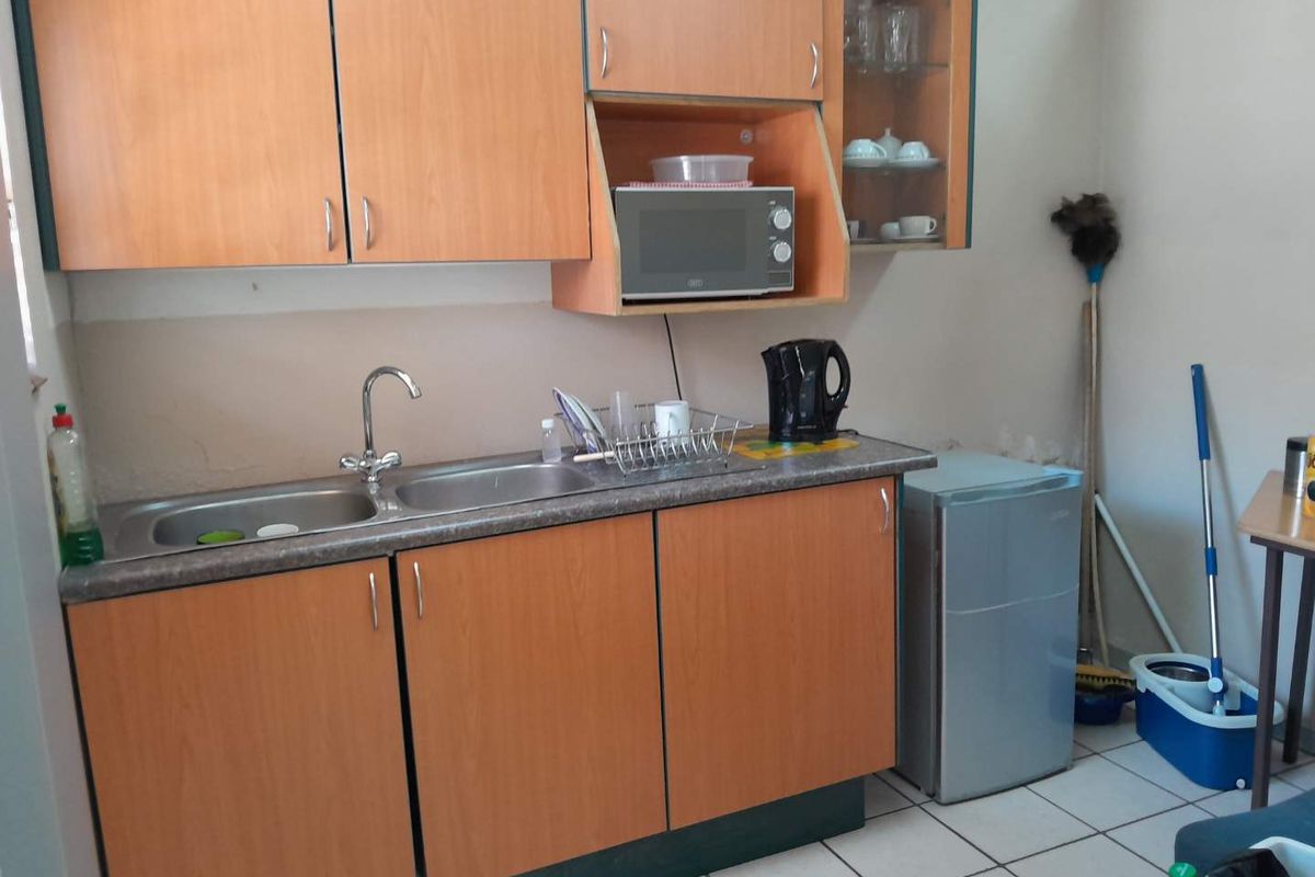 A compact kitchen area featuring laminate cabinetry, a stainless steel double sink, and tiled flooring, requiring cosmetic updates to improve its overall condition.