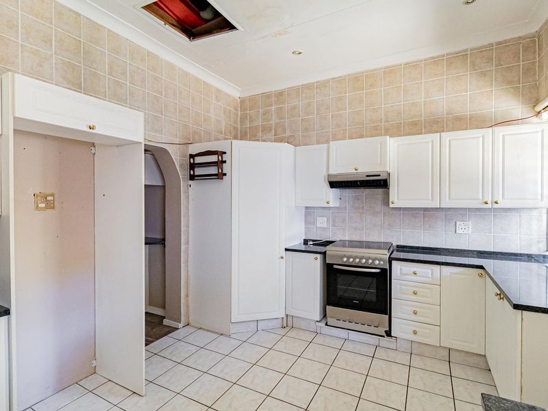A dated kitchen featuring white cabinetry, granite countertops, and tiled finishes, currently requiring ceiling repairs and general cosmetic updates.