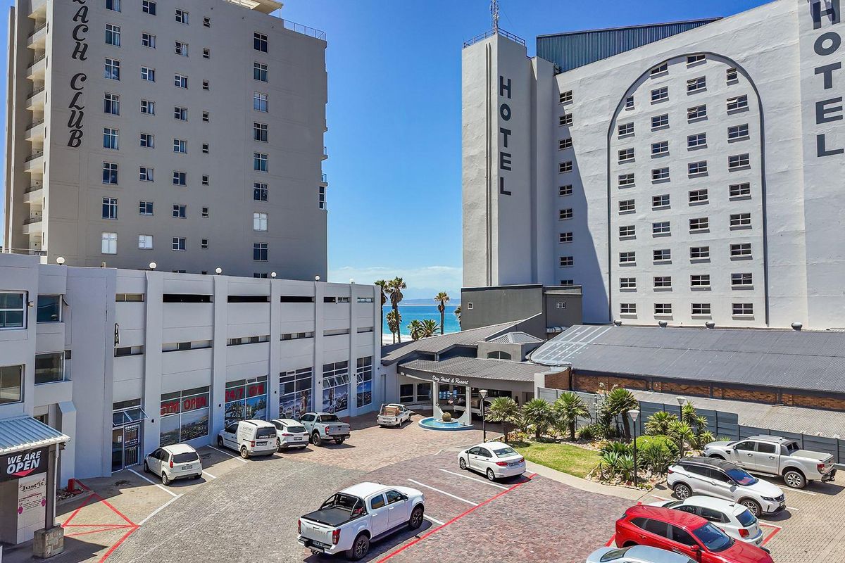 Aerial view of the hotel complex entrance, featuring paved parking areas, landscaped garden beds, and multi-story building facades.