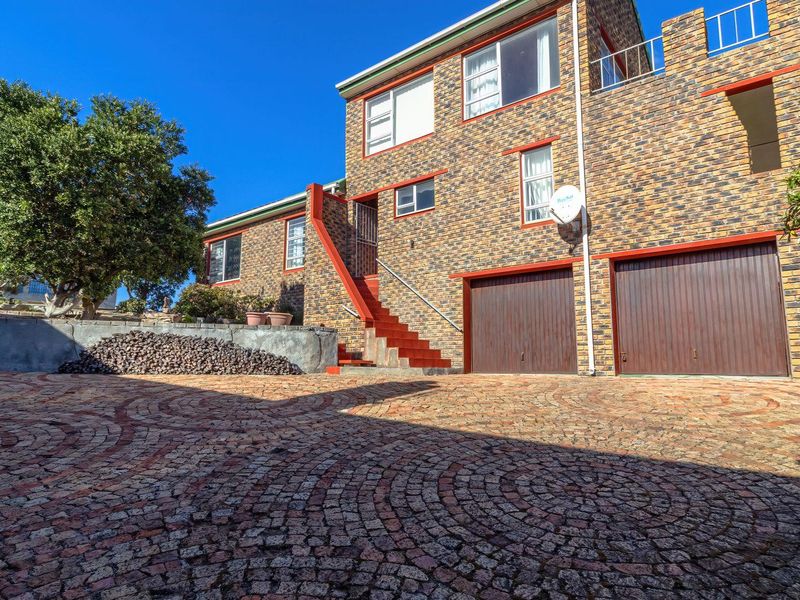 Front exterior view of a multi-level brick house featuring a double garage, paved driveway, and an external staircase leading to the upper level.