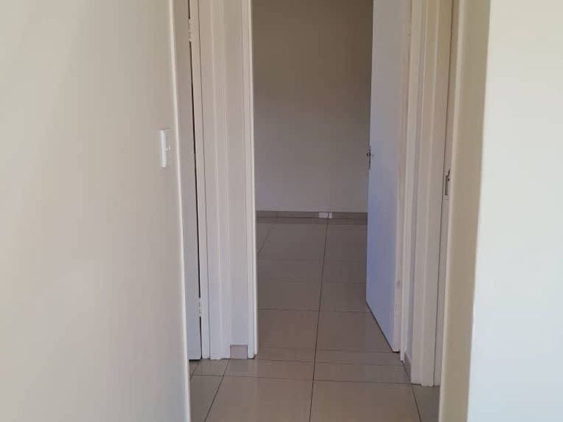 A clean, neutral-toned hallway featuring tiled flooring and coved ceilings, providing access to adjacent rooms.