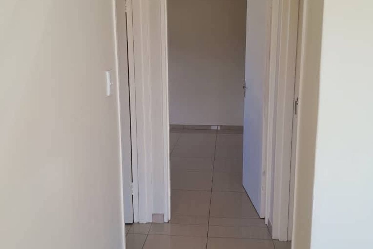 A clean, neutral-toned hallway featuring tiled flooring and coved ceilings, providing access to adjacent rooms.