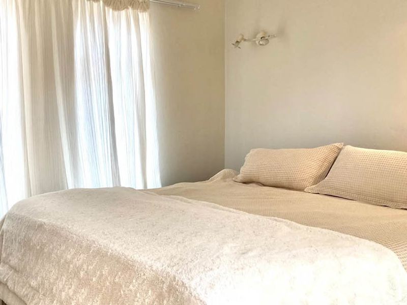 A neutral-toned bedroom featuring a wall-mounted light fixture and a curtain rail, offering a simple and functional space.
