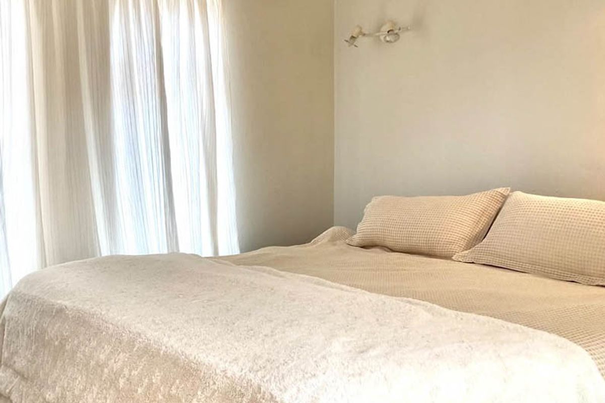 A neutral-toned bedroom featuring a wall-mounted light fixture and a curtain rail, offering a simple and functional space.