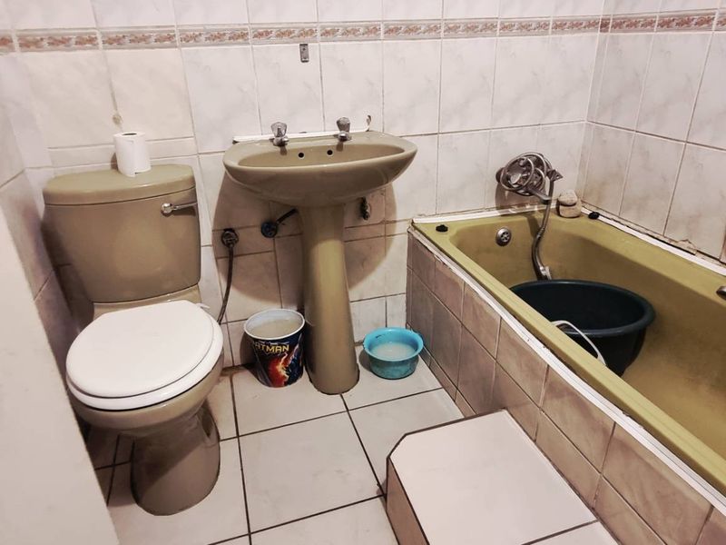 A dated bathroom featuring a pedestal basin, toilet, and bathtub with tiled walls and flooring, offering significant potential for modernization and renovation.