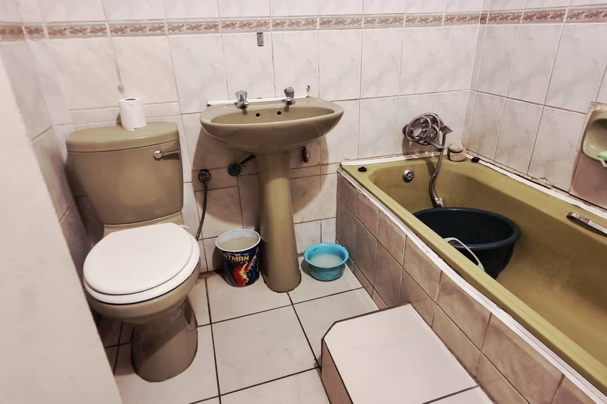 A dated bathroom featuring a pedestal basin, toilet, and bathtub with tiled walls and flooring, offering significant potential for modernization and renovation.