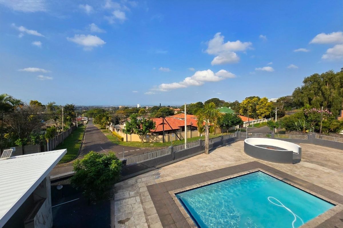 Elevated aerial view of the property featuring a swimming pool, paved patio area, and surrounding residential neighborhood landscape.