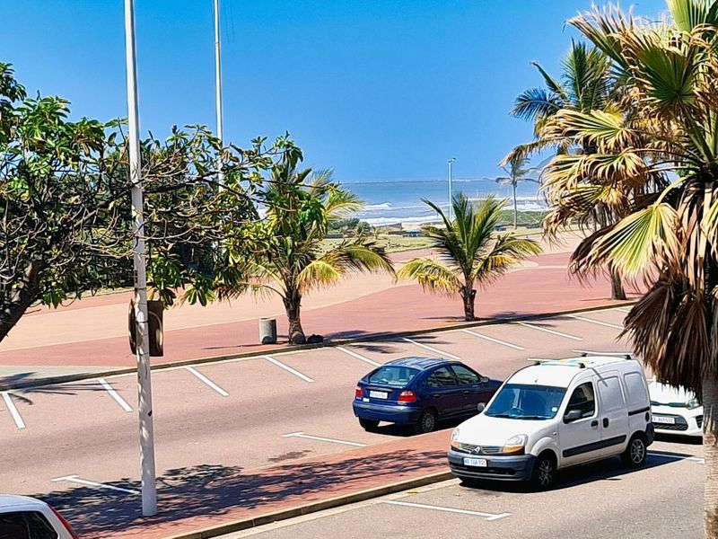 A scenic elevated view overlooking a coastal parking area, palm trees, and the ocean horizon.