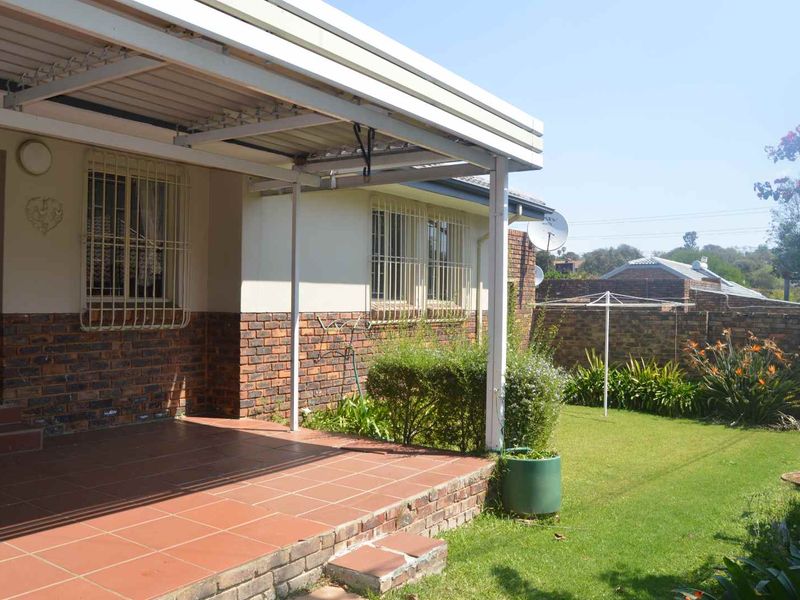 A rear view of the townhouse featuring a covered tiled patio, brick exterior walls, security bars on windows, and a well-maintained private garden.