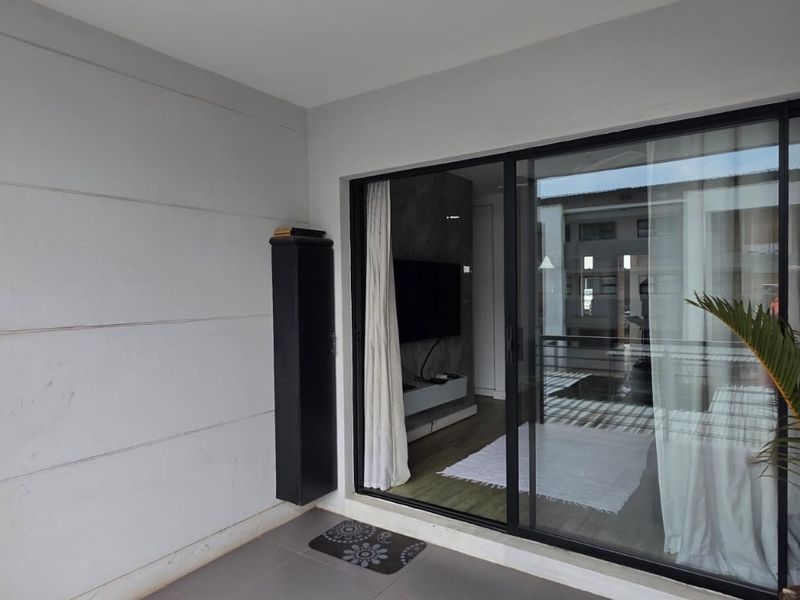A clean, covered balcony featuring tiled flooring, a modern sliding glass door, and metal safety railings, providing a seamless transition to the interior living space.