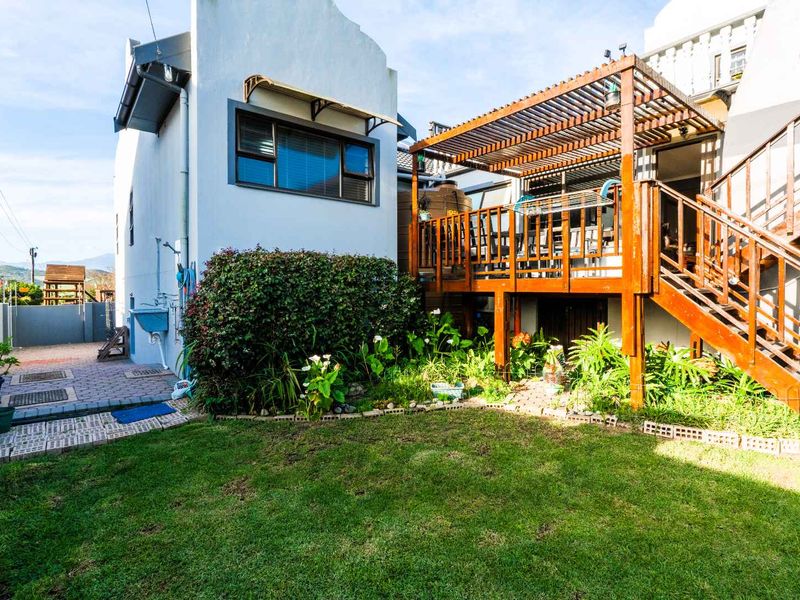 Rear garden area featuring a raised timber deck with a pergola, external staircase, paved pathways, and a small lawn area.
