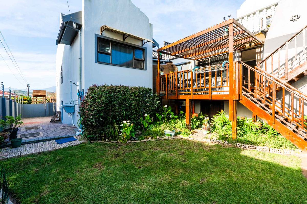 Rear garden area featuring a raised timber deck with a pergola, external staircase, paved pathways, and a small lawn area.