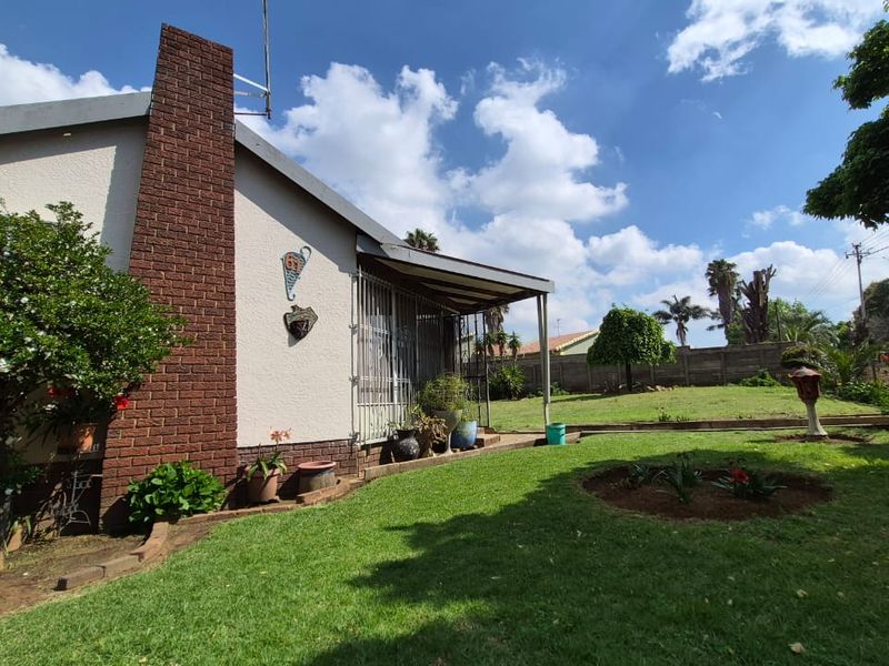 Rear view of the property featuring a brick chimney, a covered patio area, and a well-maintained garden with a boundary wall.