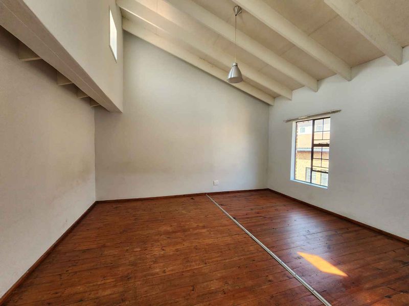 An empty living room featuring a high vaulted ceiling with exposed timber rafters and warm-toned timber flooring, offering a bright and spacious atmosphere.
