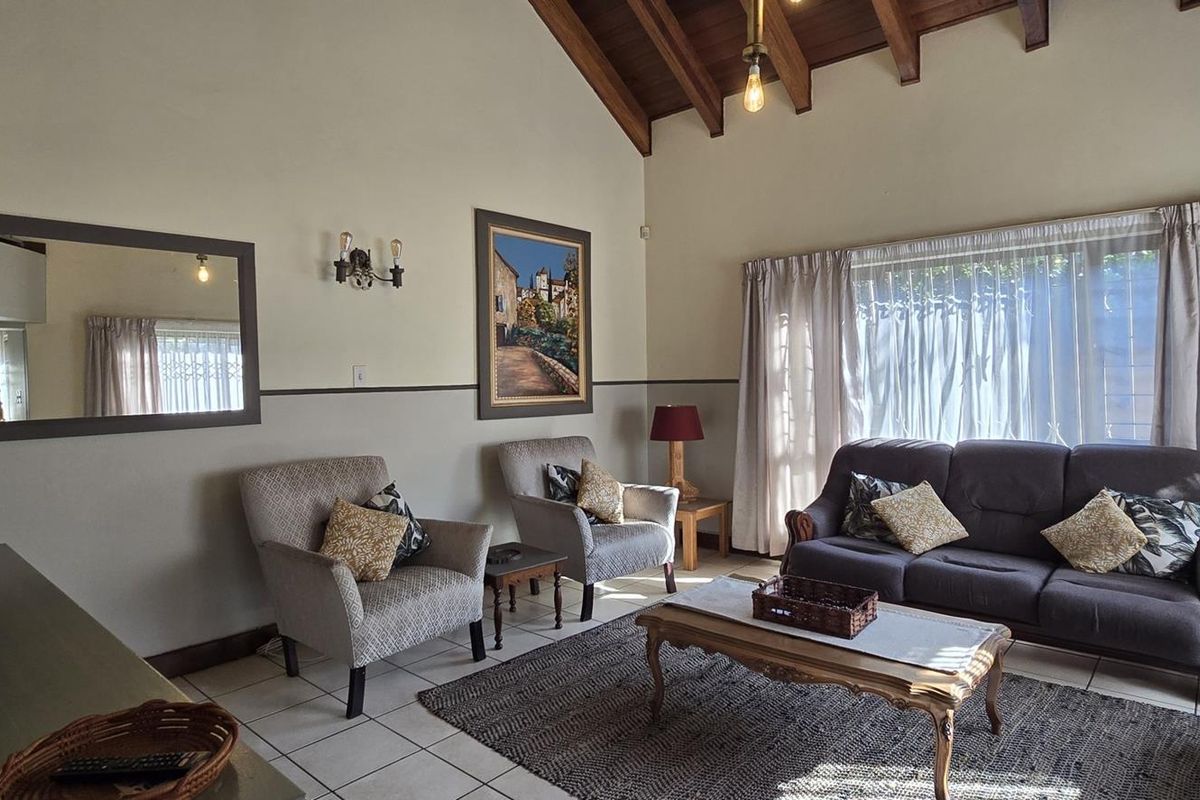 A spacious living room featuring a high vaulted timber ceiling with exposed beams, tiled flooring, and large windows allowing for natural light.