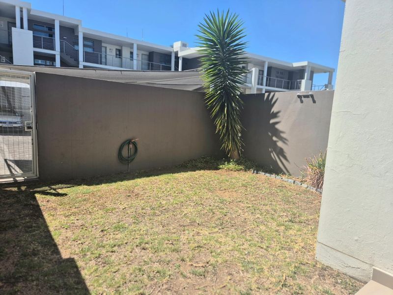 A private rear garden area featuring a lawn, boundary wall, and external water connection, providing a compact outdoor space for the apartment.