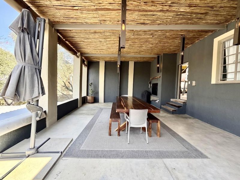 A spacious covered patio featuring a thatched roof, concrete flooring, and a built-in fireplace, ideal for outdoor dining and entertaining.