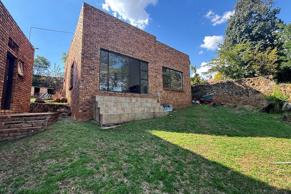 Rear view of a face-brick house featuring large windows, a tiled step entrance, and a surrounding garden with stone boundary walling.
