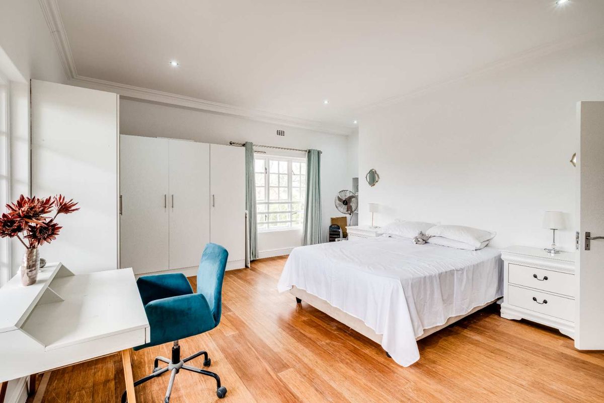 Spacious bedroom featuring polished hardwood flooring, built-in cupboards, and ample natural light through a classic multi-pane window.