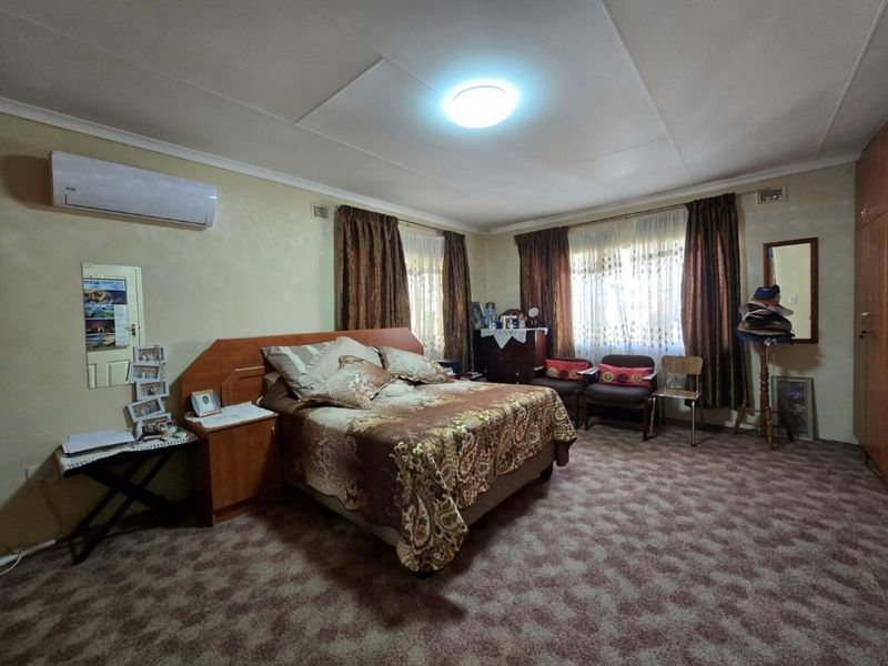 Spacious bedroom featuring built-in cupboards, carpeted flooring, and a wall-mounted air conditioning unit.