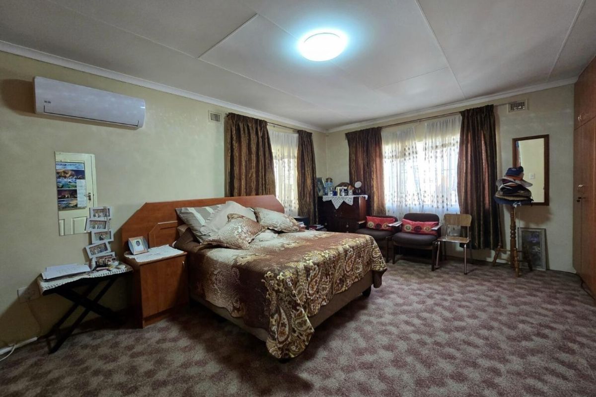 Spacious bedroom featuring built-in cupboards, carpeted flooring, and a wall-mounted air conditioning unit.