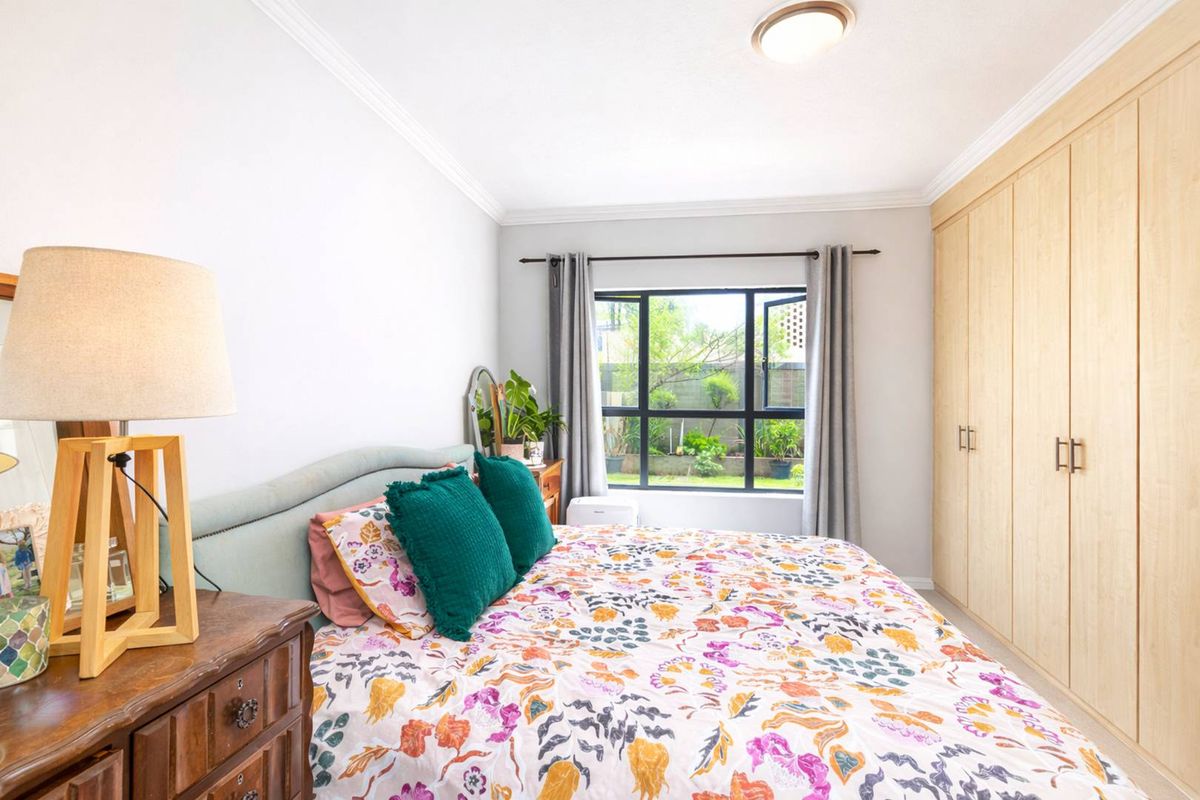 A bright bedroom featuring built-in light wood cabinetry, crown molding, and a window overlooking the garden.