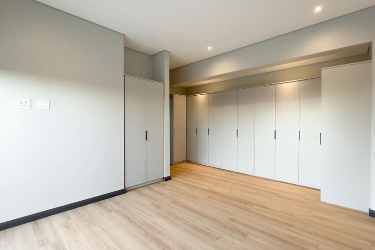 A bright, modern bedroom featuring extensive built-in cabinetry, light wood-look flooring, and recessed ceiling lighting.
