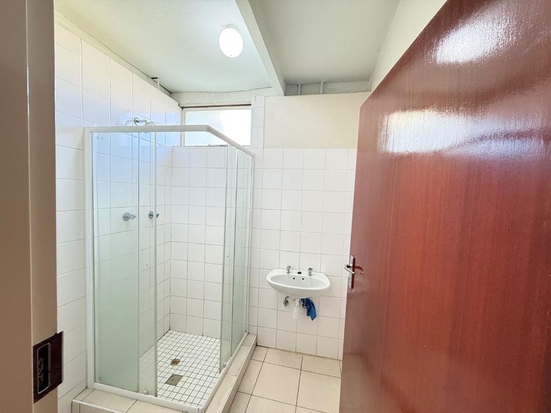 A functional bathroom featuring a glass shower enclosure, wall-mounted basin, and white tiled finishes throughout.
