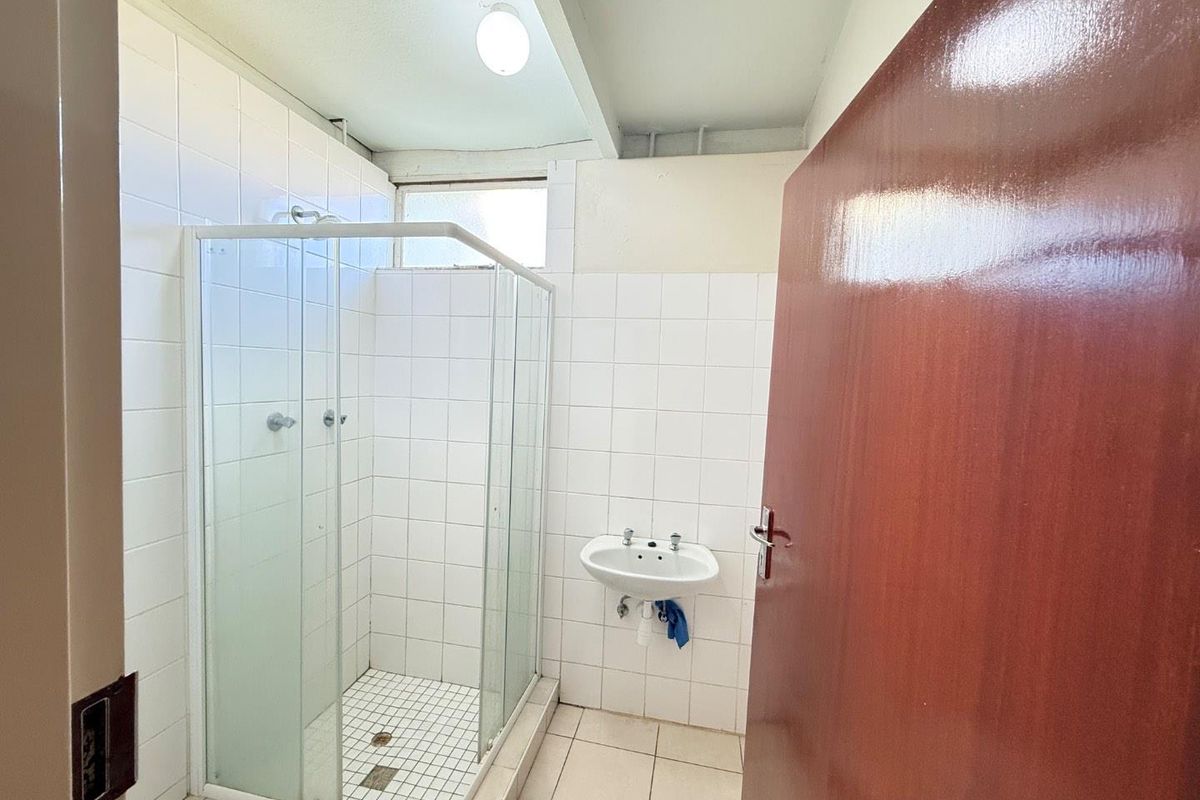 A functional bathroom featuring a glass shower enclosure, wall-mounted basin, and white tiled finishes throughout.