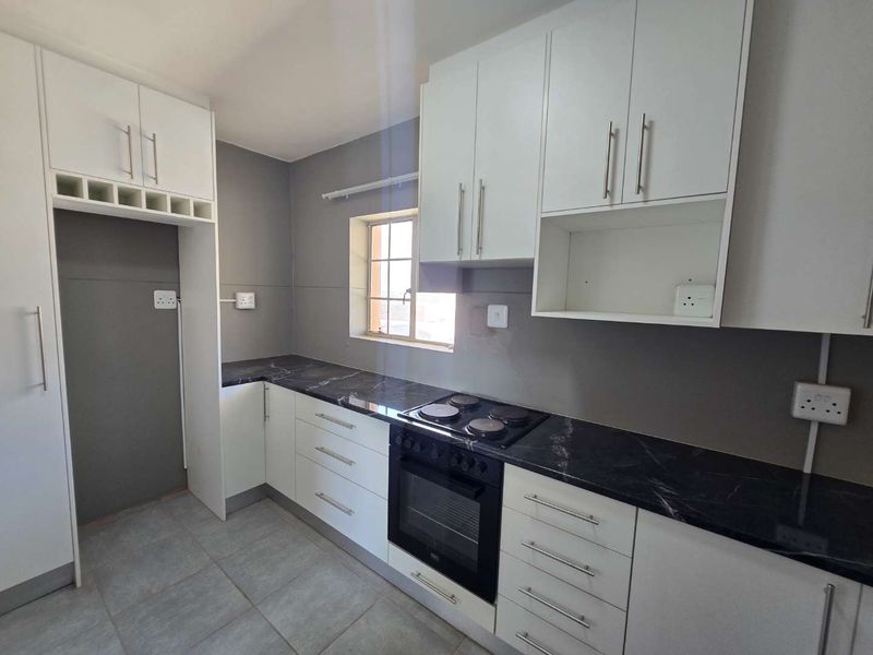 A clean, modern kitchen featuring white cabinetry, dark marble-look countertops, an integrated electric hob and oven, and neutral tiled flooring.