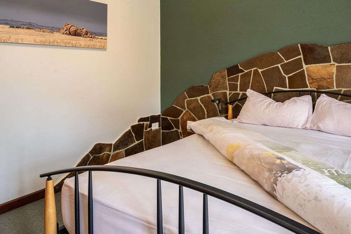 A bedroom featuring a unique stone-clad accent wall behind the bed area, creating a rustic focal point within the room.