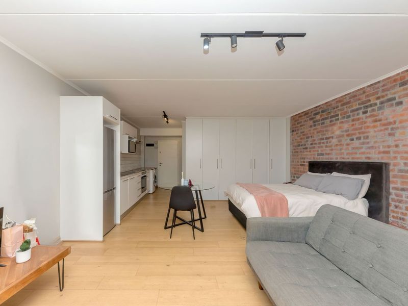 Modern open-plan studio apartment featuring laminate flooring, an exposed brick feature wall, ample built-in storage, and a functional kitchen area.