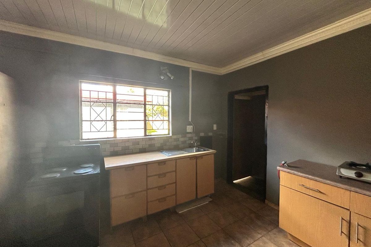 A functional kitchen featuring wooden cabinetry, tiled flooring, a built-in sink, and a window with security bars, providing a practical workspace.