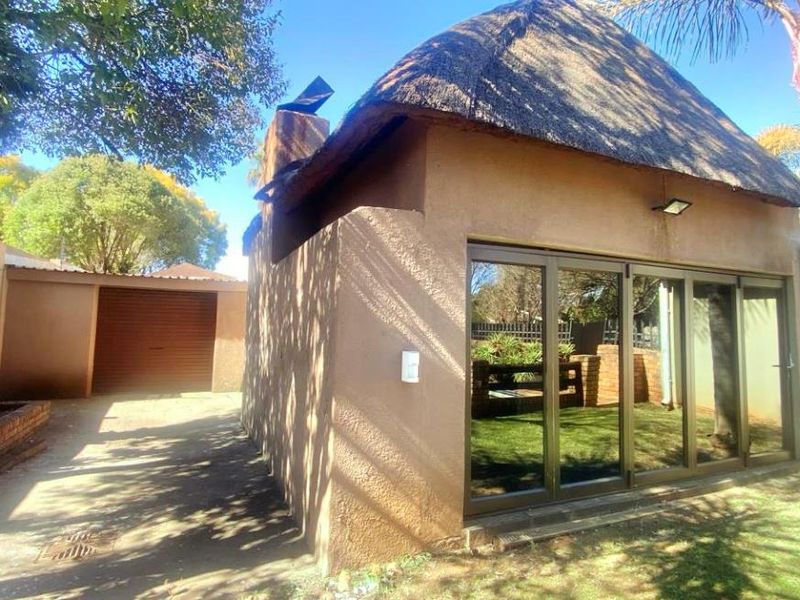 Rear view of the property featuring a thatch-roofed structure with modern aluminium stacker doors, adjacent to a paved driveway and garage.