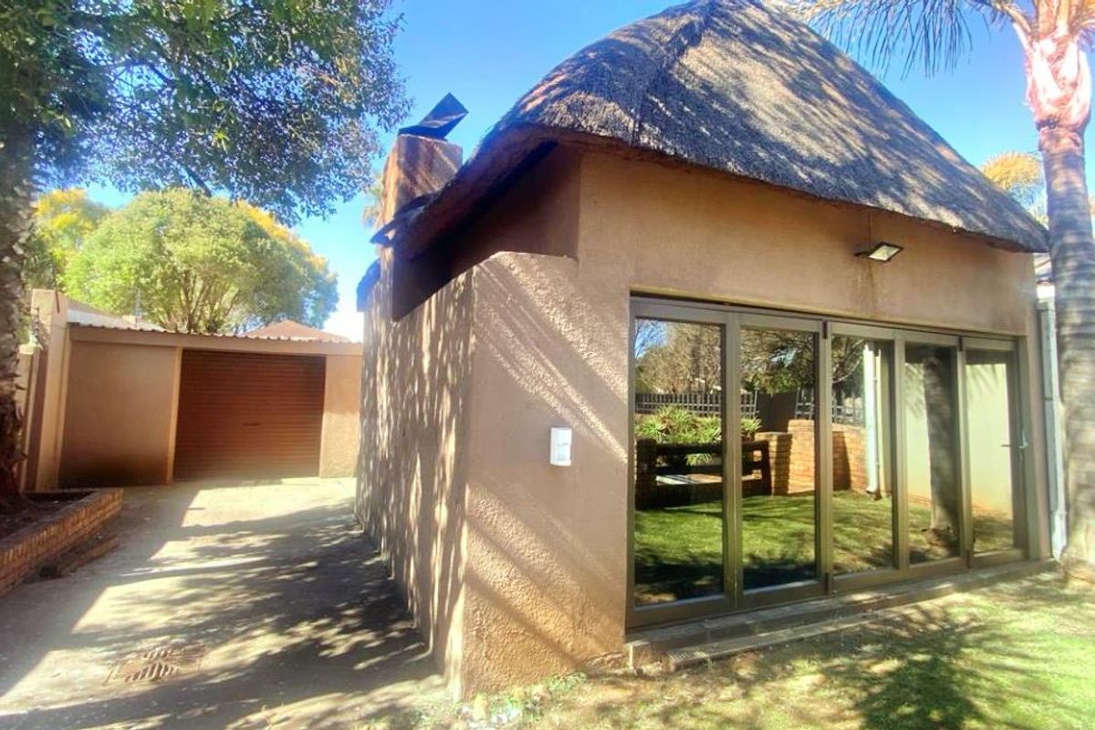 Rear view of the property featuring a thatch-roofed structure with modern aluminium stacker doors, adjacent to a paved driveway and garage.