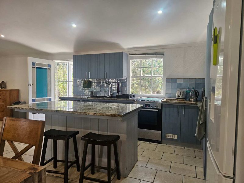 A functional kitchen featuring a central island with granite countertops, blue cabinetry, tiled backsplash, and built-in cooking appliances.