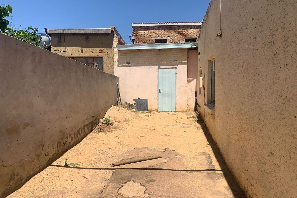 A narrow exterior rear courtyard area featuring concrete paving, perimeter boundary walls, and access to a rear building entrance.